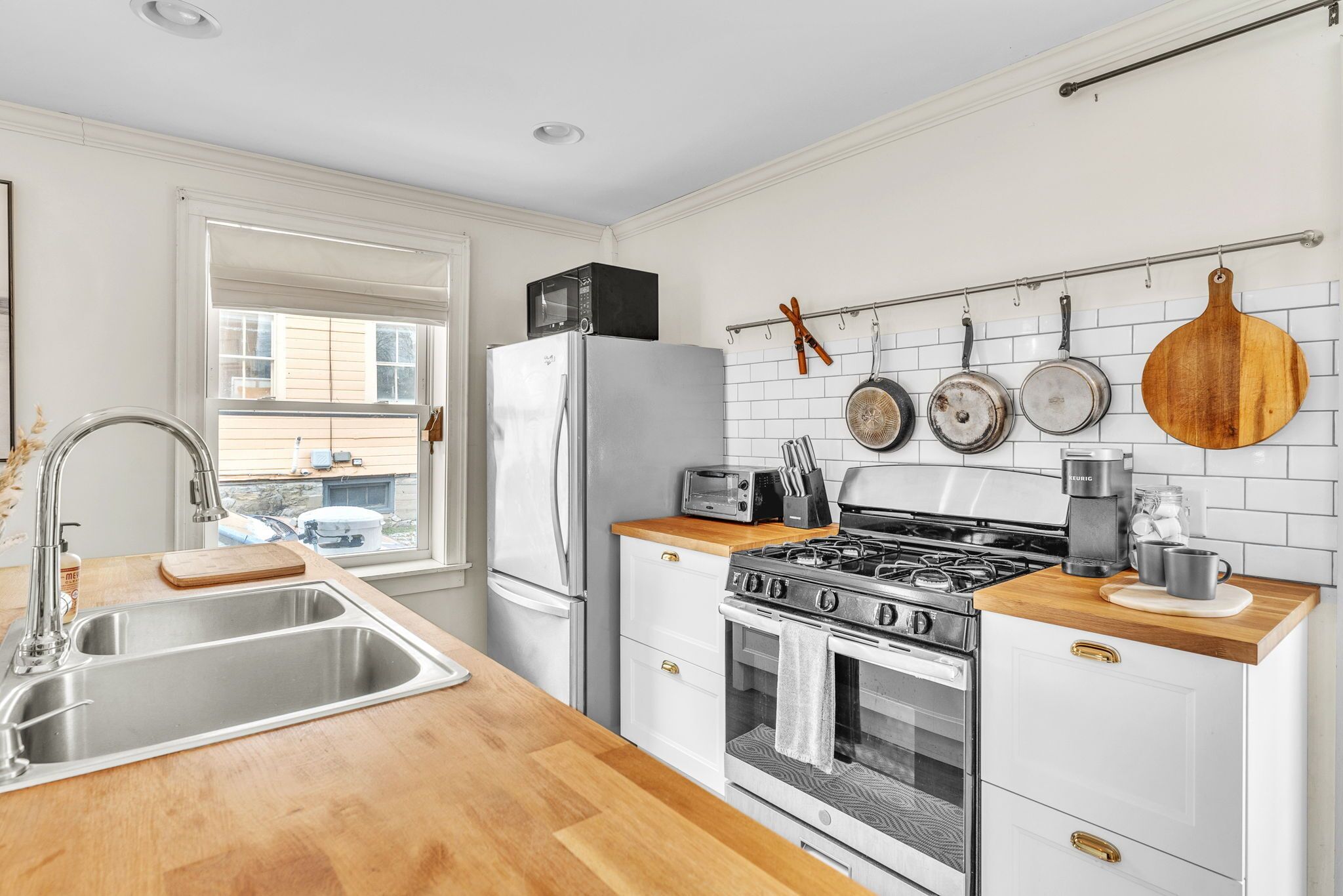 Una cocina moderna con un lavamanos de acero inoxidable, armarios blancos, encimera de madera, estufa a gas y refrigerador.
