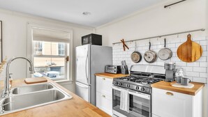 Een moderne keuken met een roestvrijstalen spoelbak, witte kasten, een houten aanrecht, een gasfornuis en een koelkast.