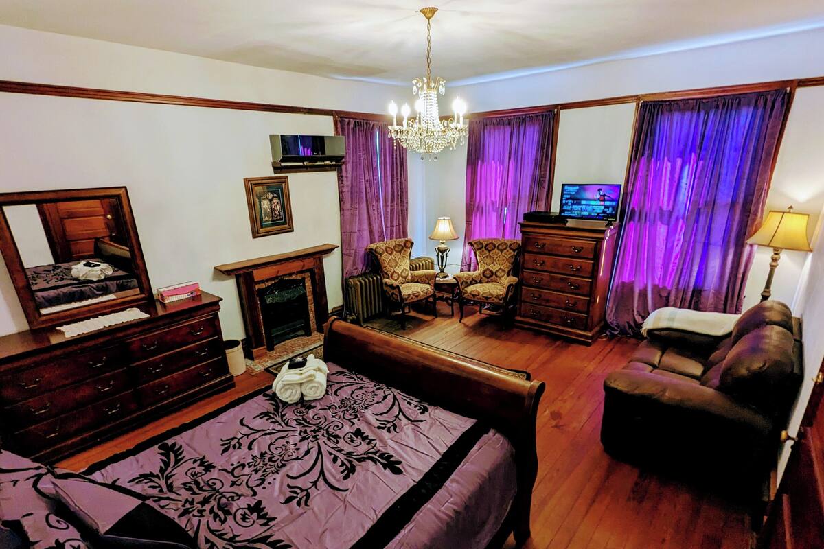 A traditional room with a bed, a dresser, a chair, a sofa, a fireplace, and a television.