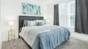 A bedroom with a bed, a nightstand, a ceiling fan, a window with curtains, and a wall-mounted abstract painting.