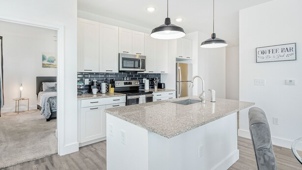 A modern kitchen with white cabinets, a granite countertop, stainless steel appliances, and pendant lighting.