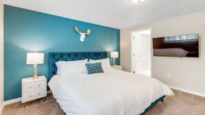 A bedroom with a teal accent wall, a tufted headboard, a white bedspread, a decorative moose skull, and a mounted television.