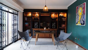 Un coin repas comprenant une table en bois, deux chaises, un luminaire suspendu et une bibliothèque remplie de divers objets.