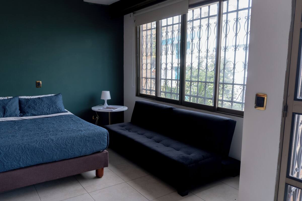 Une chambre à coucher avec un lit, une table de chevet avec une lampe, un banc et une fenêtre donnant sur l’extérieur.