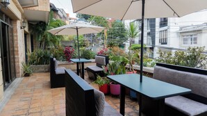 Une terrasse extérieure aménagée avec des sièges et des parasols, entourée de plantes en pot et offrant une vue sur les bâtiments.
