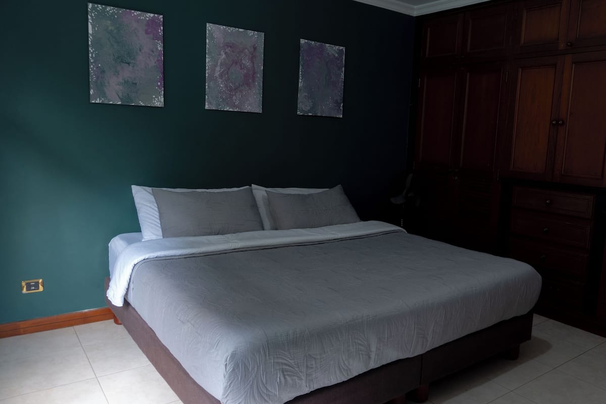 Une chambre à coucher avec un lit, une armoire et trois tableaux abstraits accrochés au mur.