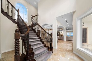 Un magnifique escalier en bois, doté d’une rampe en bois et de balustrades en métal, mène à un vaste espace de vie offrant une vue sur l’extérieur.