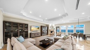 Een ruime woonkamer met een grote beige modulaire bank, een flatscreen-tv en een open haard.