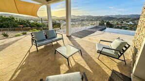 Une terrasse couverte, aménagée avec du mobilier d’extérieur, offrant une vue sur un lac et sur des montagnes lointaines.