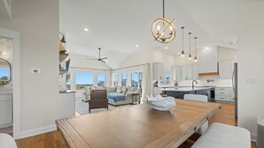 A spacious living area with a wooden dining table, a large window, and a view of the outdoors. - Wags & Waves: Sept. 18th Wk Reduced, Fri-Fri, Dog-friendly, Walk to Beach (Corolla)