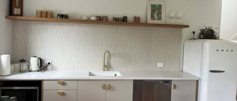 Una cocina moderna con armarios blancos, un microondas de acero inoxidable, un refrigerador blanco y un estante de madera sobre el fregadero.