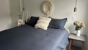 Une chambre à coucher avec un grand lit, une table de chevet, une lampe fixée au mur et un petit vase avec des fleurs.