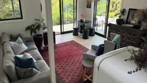 Un salon moderne avec un canapé gris, des coussins à motifs, un tapis rouge et un coin repas comprenant une table ronde et des tabourets.