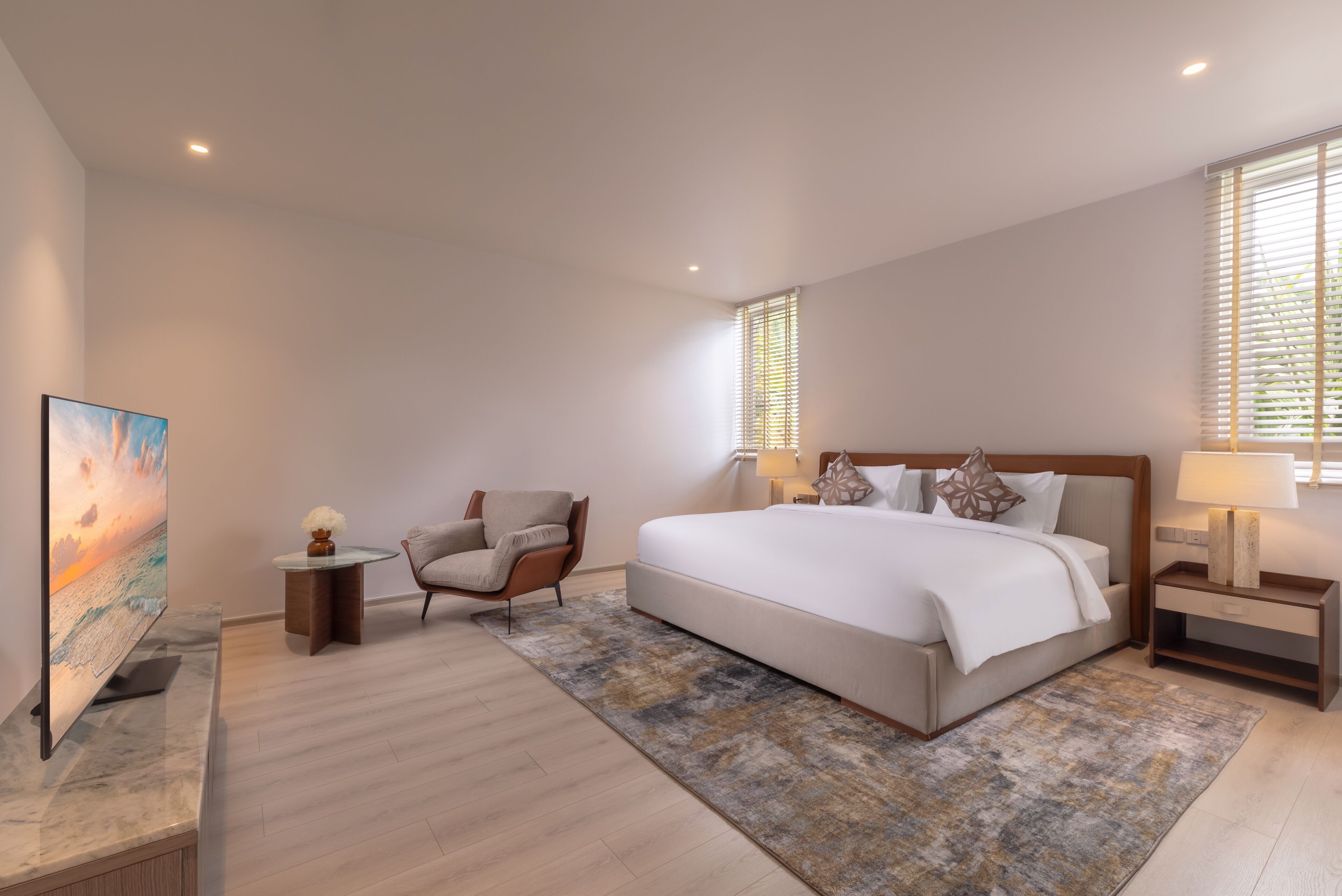 A modern bedroom with a large bed, a chair, a TV, and a painting.