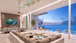 A spacious living area with a large sofa, dining table, and a TV. A balcony overlooks a scenic ocean view. - Villa AMANN (Kamala)