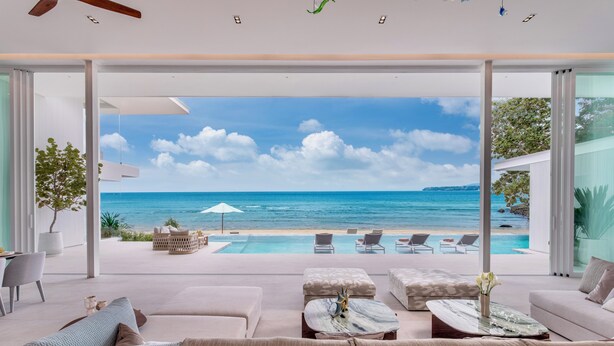 A modern living room with a large glass door leading to a pool and ocean view. - Villa AMANN (Kamala)