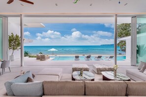 A modern living room with a large glass door leading to a pool and ocean view. - Villa AMANN (Kamala)