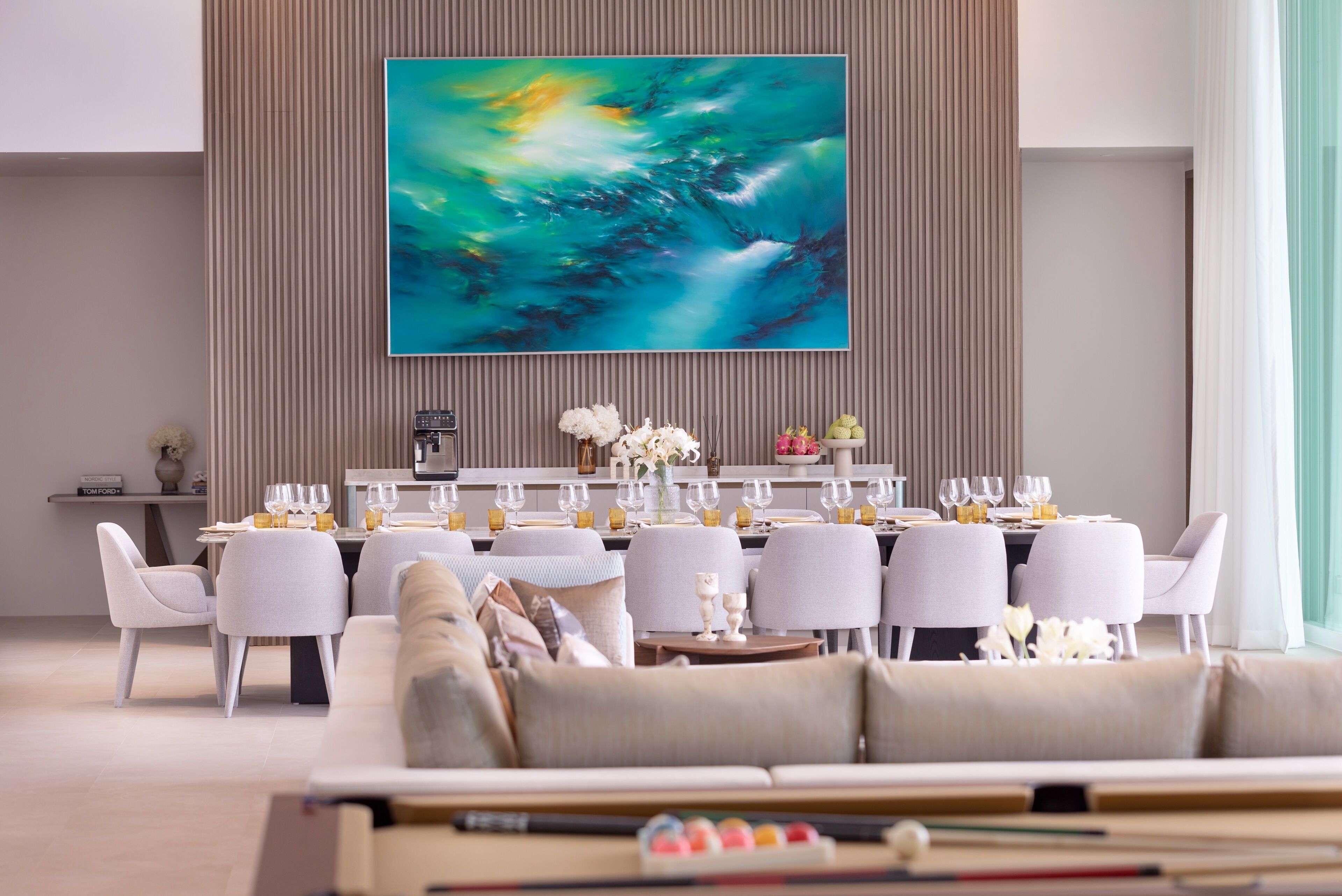 A modern dining area with a large abstract painting, white chairs, and a table set for six.