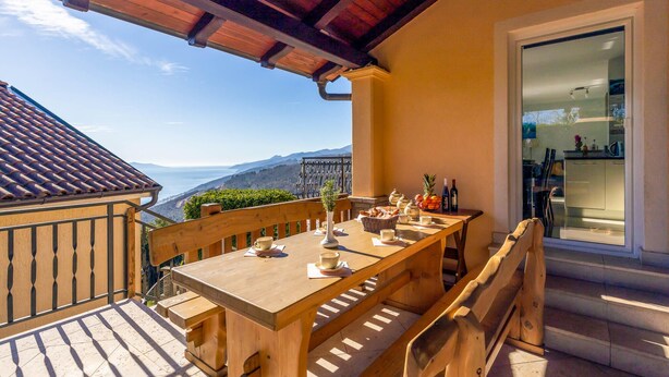 A wooden table set for dining with a view of the sea and mountains.