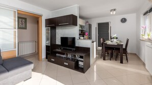 A modern living room with a flat-screen TV, built-in speakers, and a dining area with a table set for two.