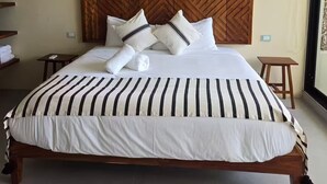 Una habitación de hotel con una cama grande, cabecera de madera, ropa de cama blanca y un ventilador de techo.