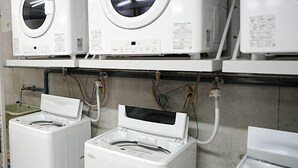 Une rangée de machines à laver blanches, dotées de panneaux de commande, est reliée à un tableau électrique fixé au mur.
