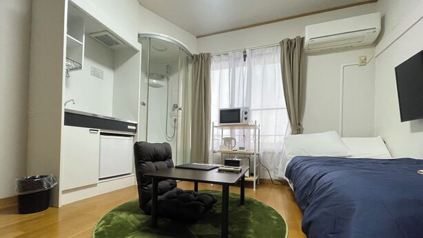 Une chambre d’hôtel compacte comprenant un lit, un bureau, une chaise, une petite kitchenette et un espace douche.