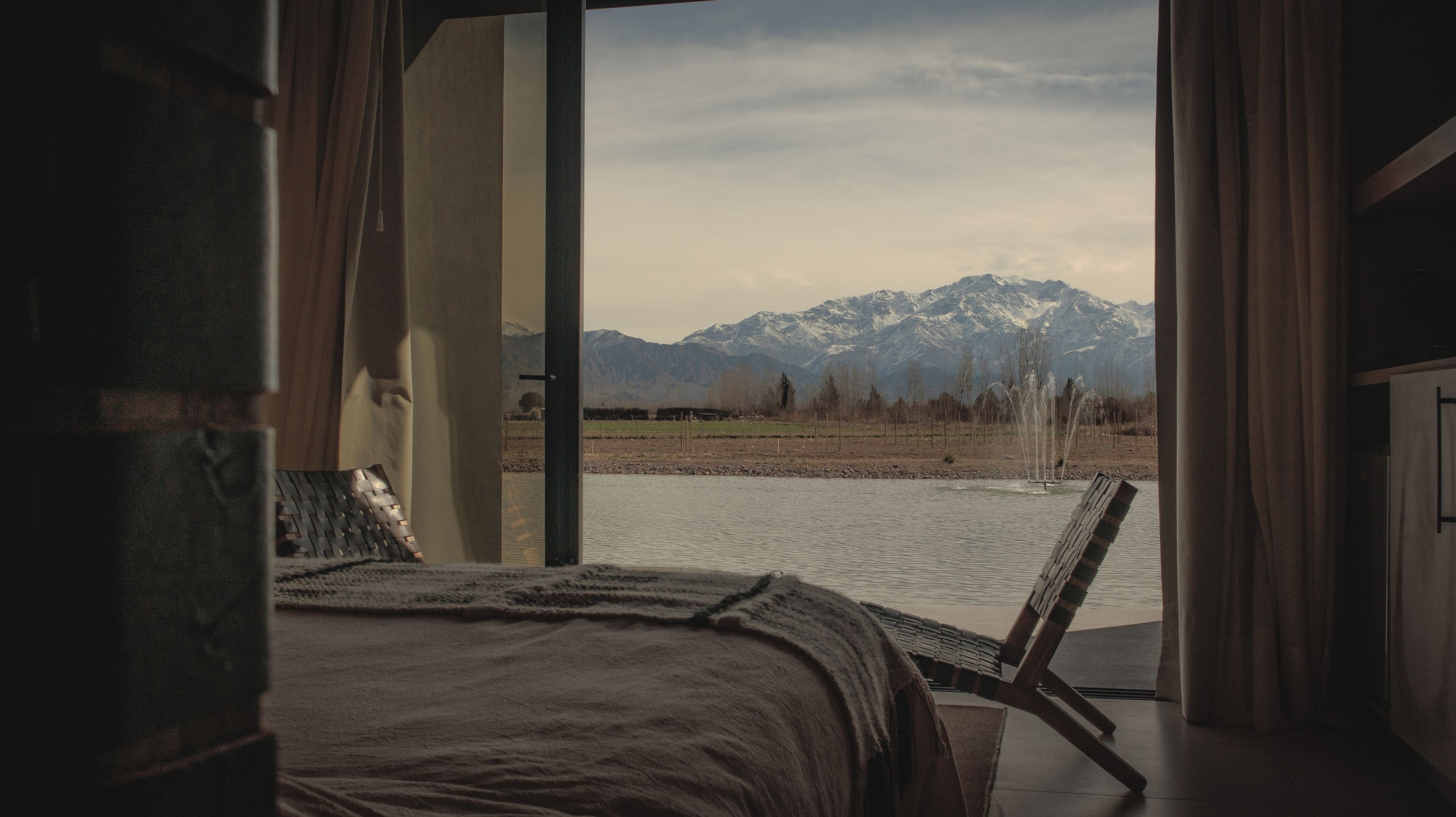 Un dormitorio con una cama, vistas a una cadena montañosa y una masa de agua.