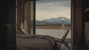 Un dormitorio con una cama, vistas a una cadena montañosa y una masa de agua.