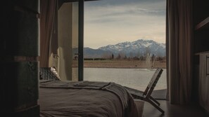 Quarto com cama, vista de uma cordilheira e um corpo de água.