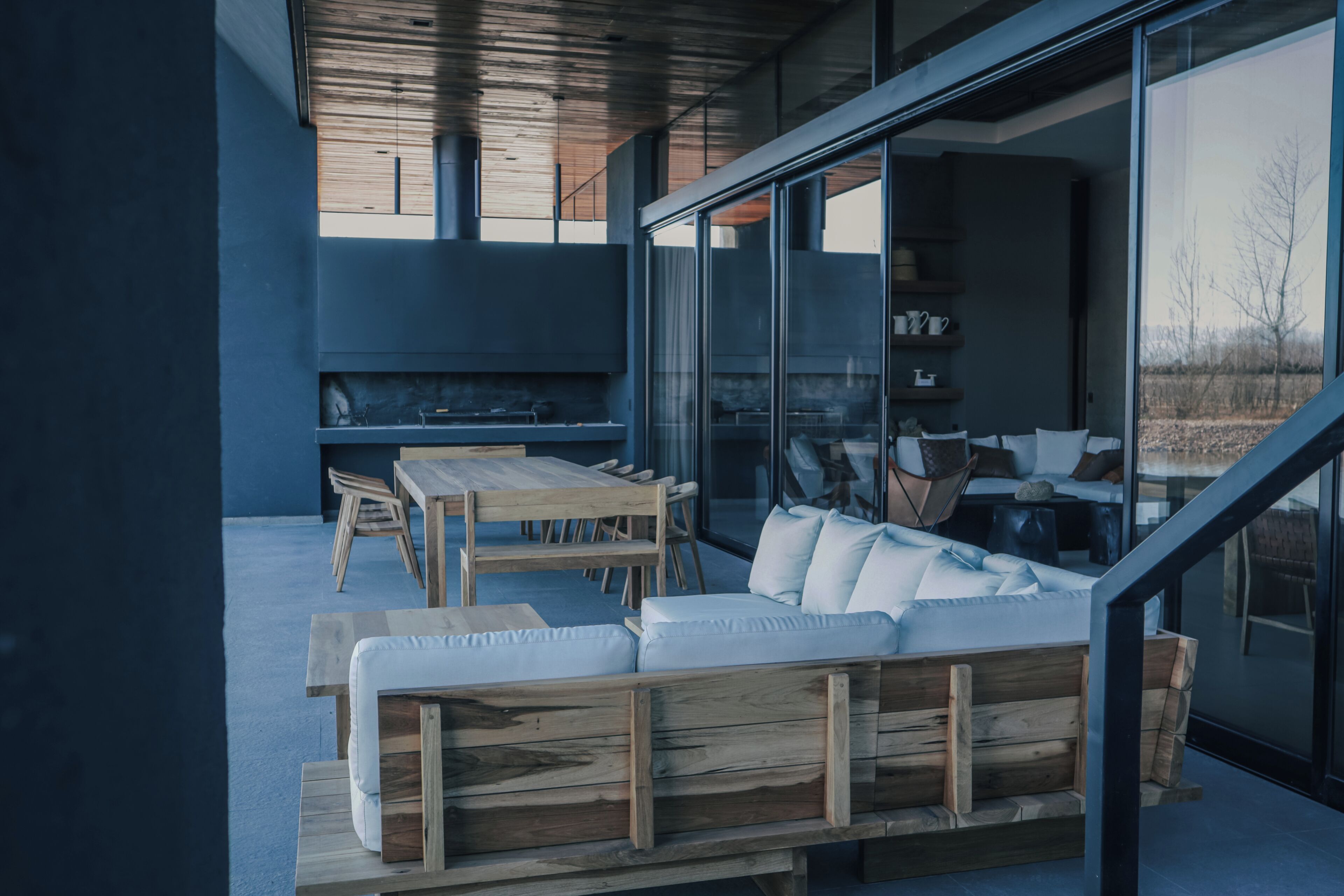 Un espace extérieur moderne, aménagé avec un banc et une table en bois, un mur en verre et une cheminée.
