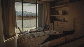 A bedroom with a large window, a bed, a chair, a small table, and a wooden cabinet. - Finca Boutique Un Buen Año (Eugenio Bustos)