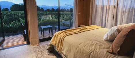Ein Schlafzimmer mit einem großen Bett, einer Holzbalkendecke und Blick auf einen Weinberg durch große Fenster.