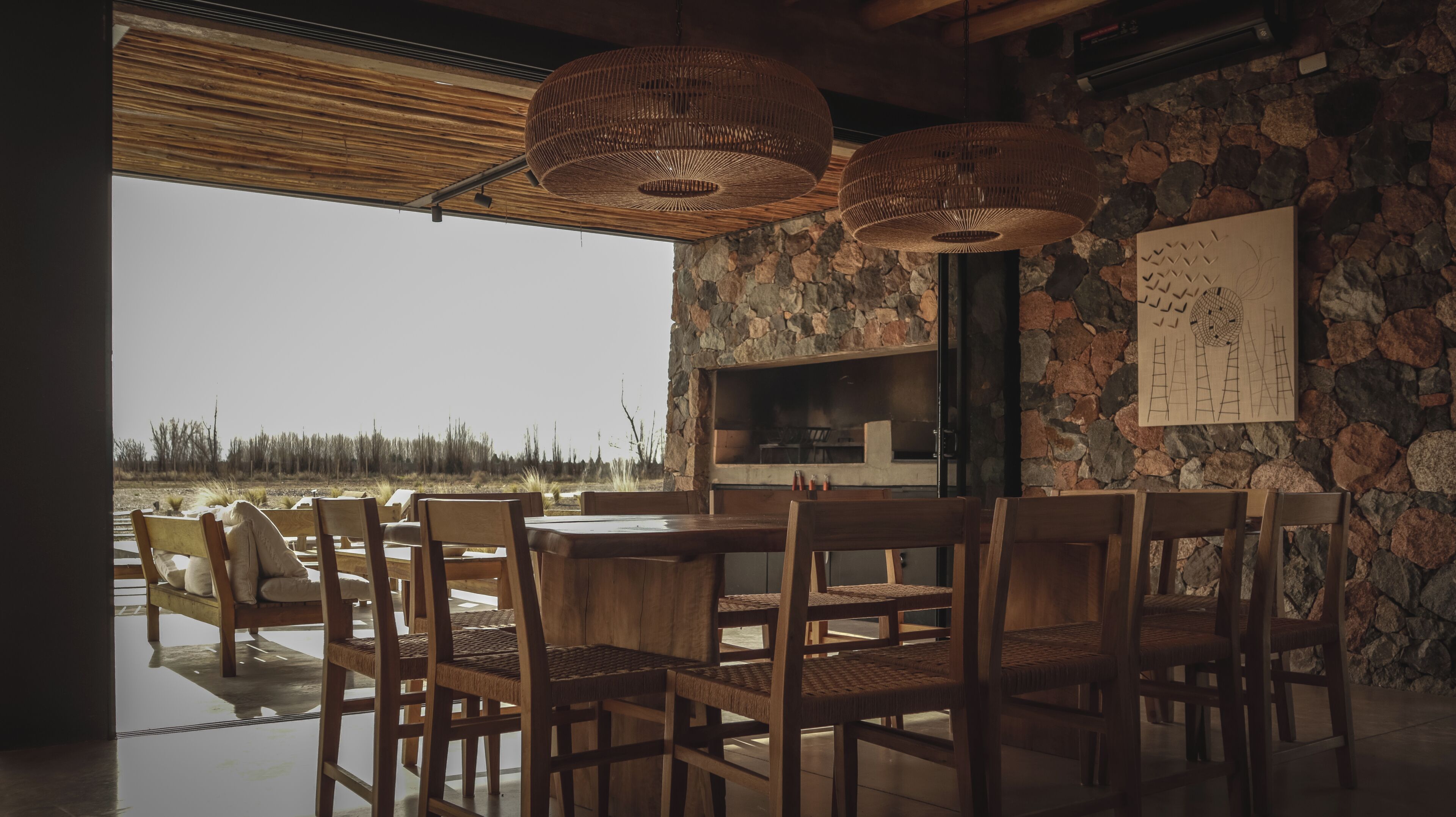 A dining area with a stone wall, wooden furniture, and a view of the landscape.