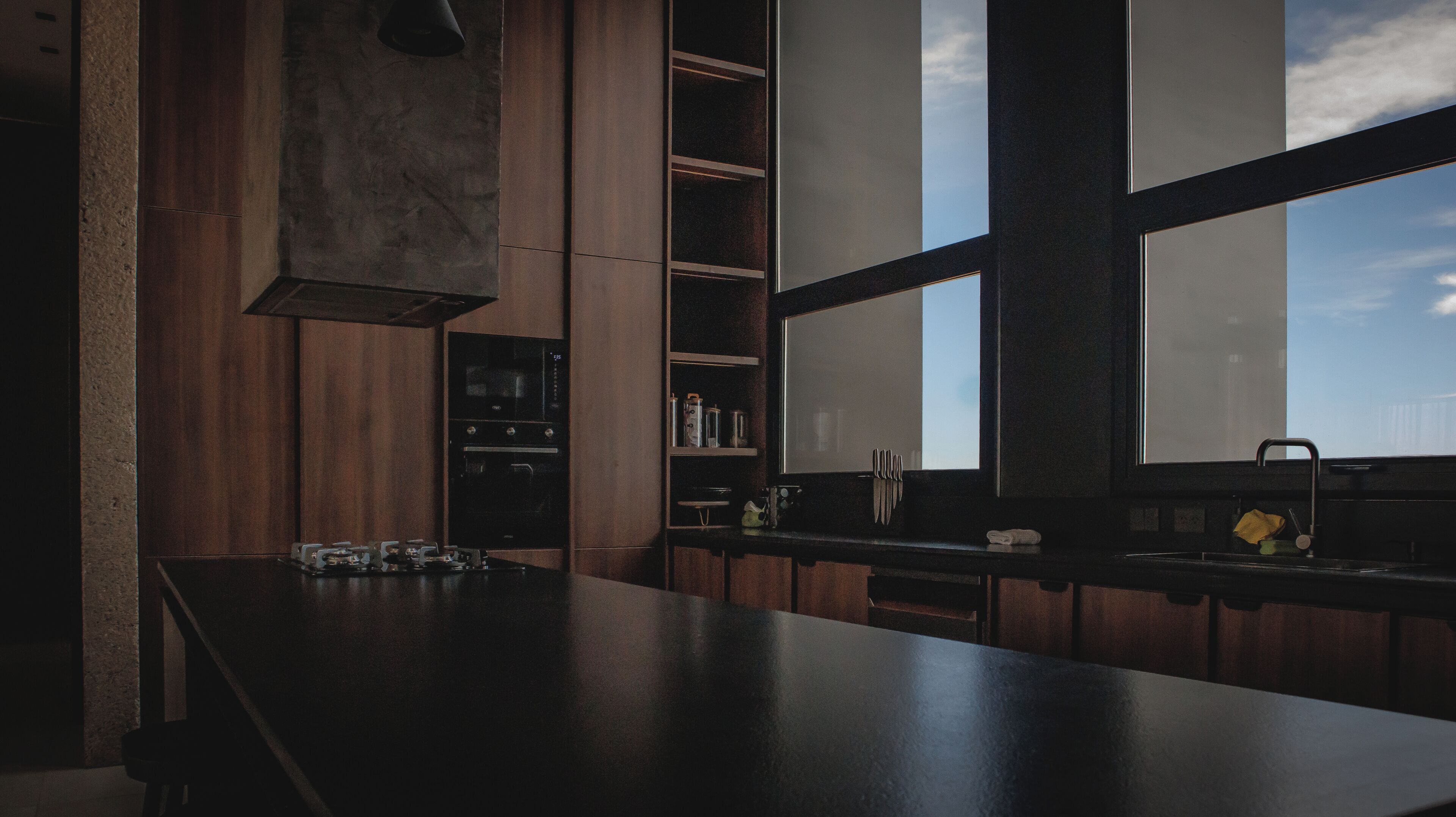 A modern kitchen with a large island, built-in shelves, and a window providing a view of the sky.