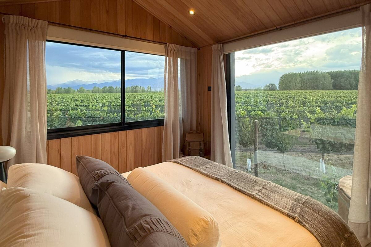 A bedroom with a large window offering a view of a vineyard.