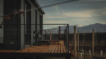 Una terraza de madera con barandilla metálica, un banco y vistas a montañas al fondo.