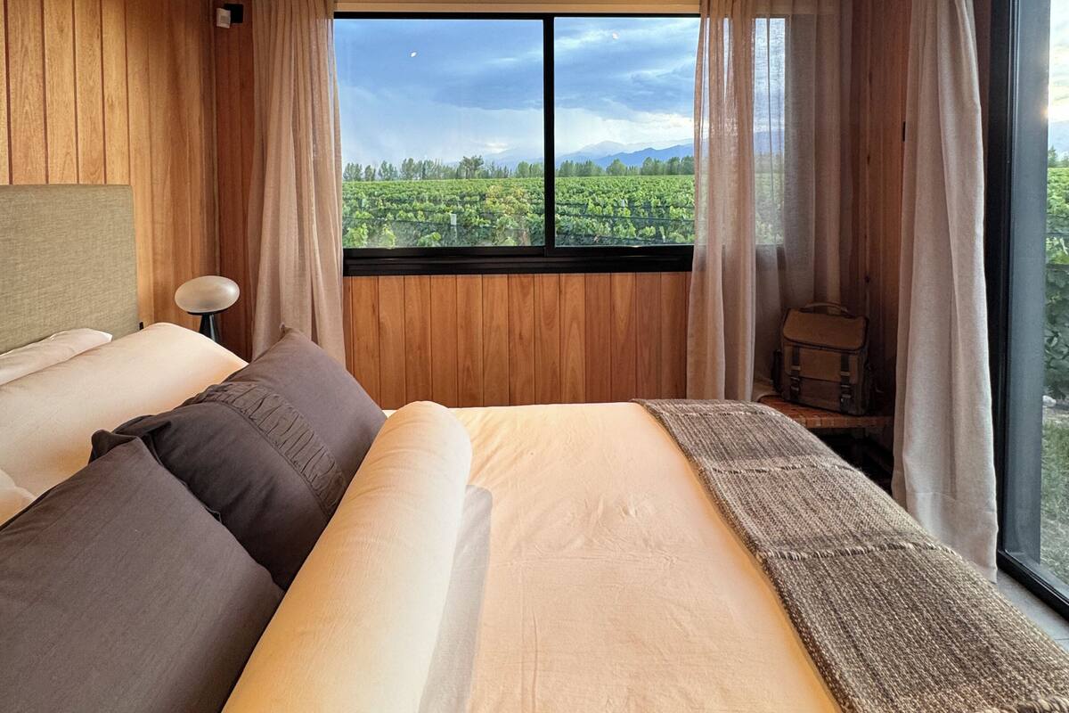 A bedroom with a large bed, wooden ceiling, and a window with a view of greenery and mountains.