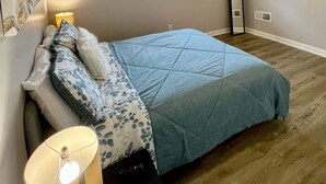 Ein Schlafzimmer mit einem Bett, einem Fenster, einem an der Wand befestigten Fernseher und einer Lampe.