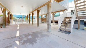 Un patio abierto con una terraza de madera, barandas blancas y una escalera que lleva a un nivel superior.