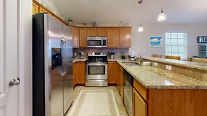 Una cocina moderna con electrodomésticos de acero inoxidable, armarios de madera, encimeras de granito e iluminación colgante.