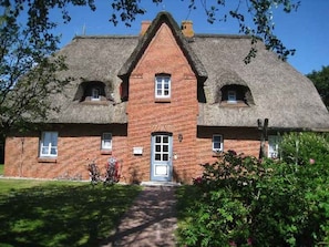 A traditional brick house with a thatched roof, a central entrance, and a small porch area. - Your vacation under thatch - Cosy first floor apartment in Wyk - Boldixumer Straße (Wyk auf Föhr)