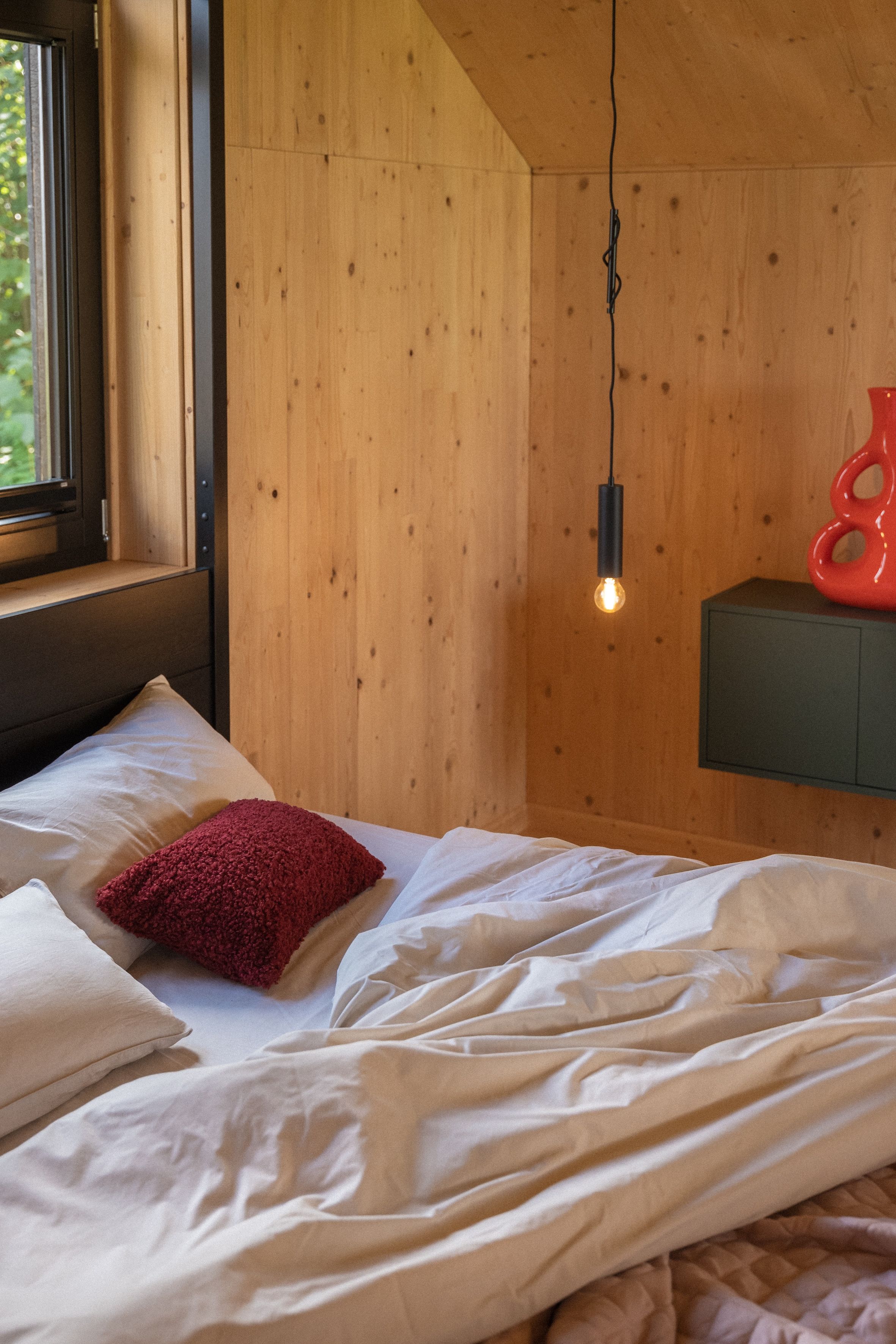 Ein Schlafzimmer mit Holzbalkendecke, einer hängenden Glühbirne, einem roten Dekorationsgegenstand und einem grünen Schrank.