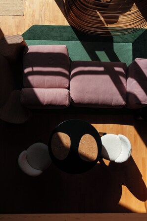 A sectional sofa with multiple cushions, a round coffee table with a cork top, and a patterned rug on a wooden floor.