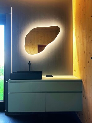 A modern bathroom with a minimalist design, featuring a wooden vanity with a built-in sink and a unique, illuminated mirror.