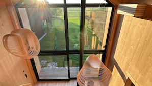 Un interior moderno con un ventanal grande, suelo de madera y un rincón de descanso acogedor con cojines.