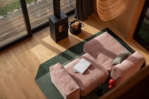 Ein gemütliches Zimmer mit Holzboden, einem rosafarbenen Sofa mit Kissen, einem Buch und einem Holzscheitkorb.