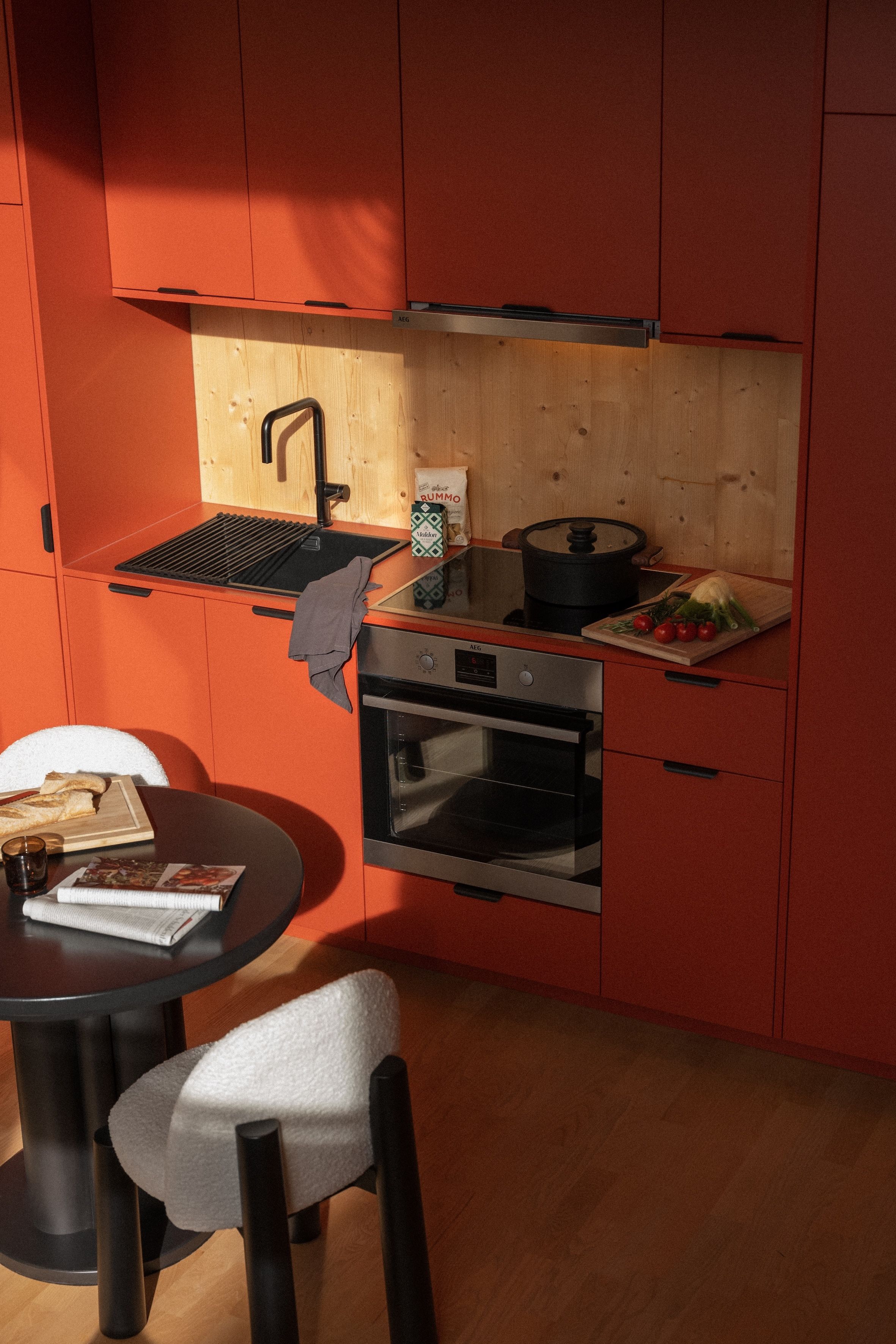 Cocina compacta con encimera de madera, pileta, cocina y comedor con mesa y sillas.