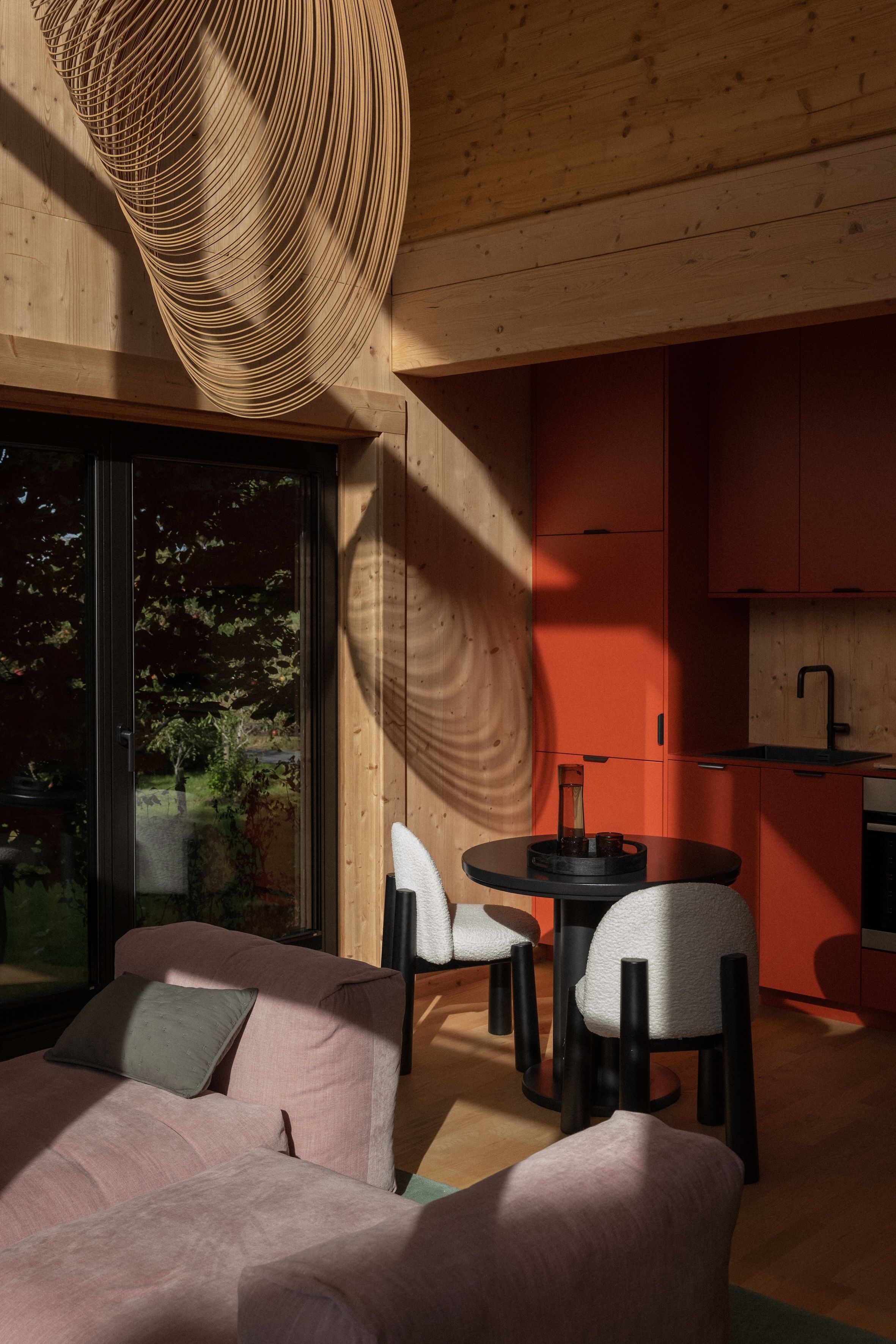 Ein modernes Interieur mit Holzbalkendecke, einem rosafarbenen Sofa und einem runden Tisch mit Stühlen.