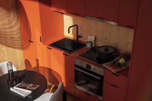 A compact kitchen with a built-in oven, a coffee maker, and a cutting board with vegetables.